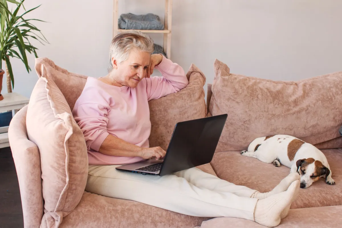 Older pet owner relaxing at home while using a laptop, with their dog resting nearby, representing online research, digital veterinary engagement, and modern pet owner behaviour.