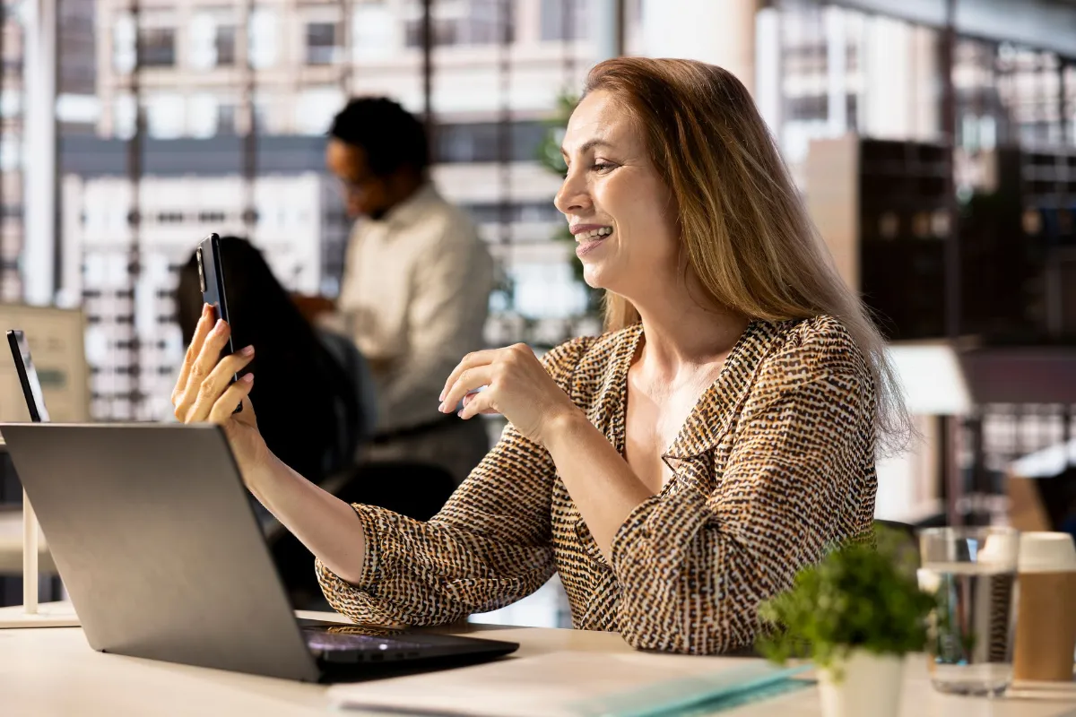 Smiling businesswoman sitting at a desk in a modern office using her smartphone.