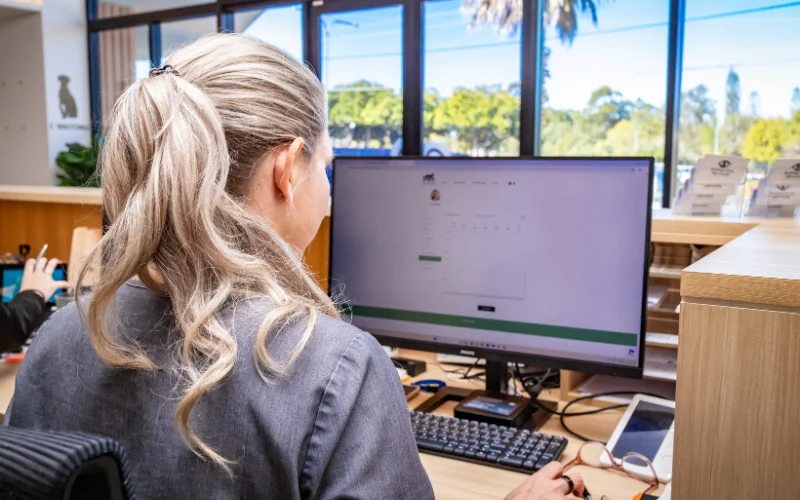 Veterinary clinic staff member using practice management software at a reception desk computer inside a modern animal hospital.